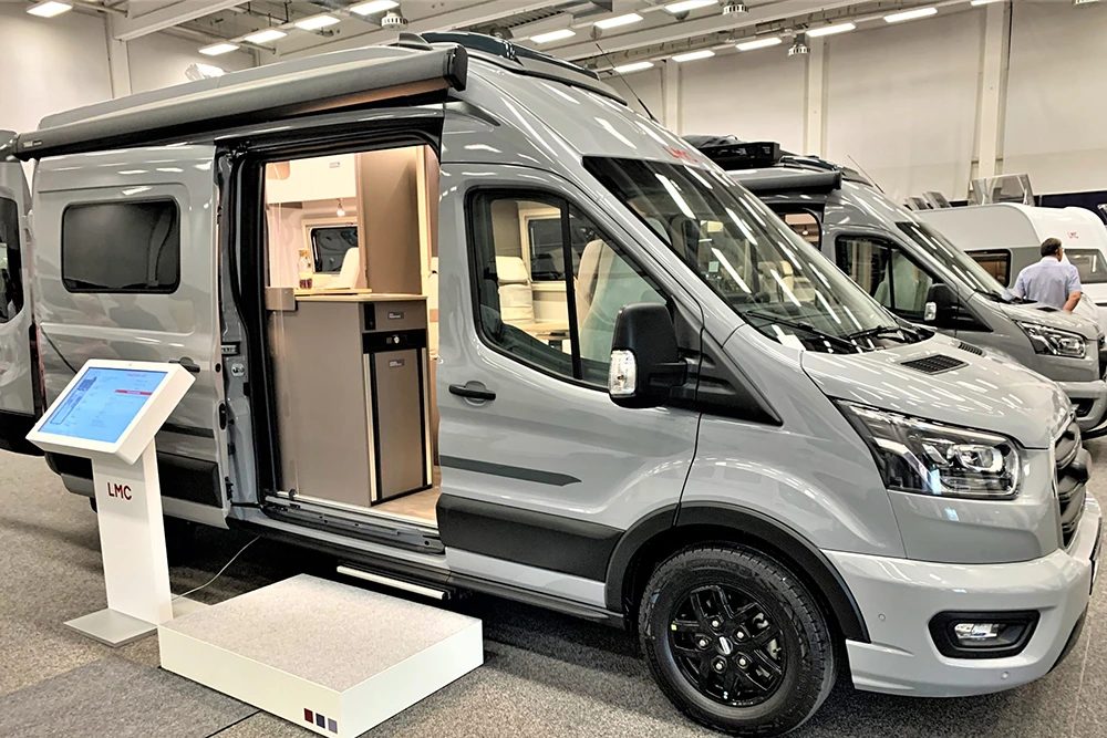 Drie campers van verschillende grootte naast elkaar op een camperplaats in de avond.