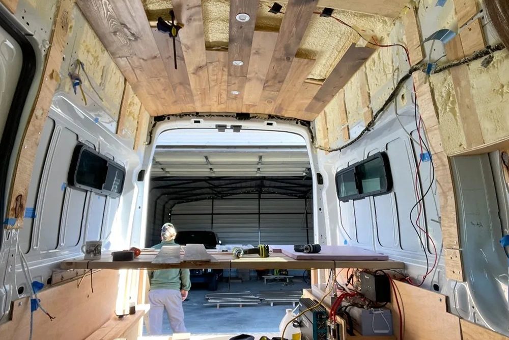 Half afgebouwde bestelbus met isolatie en regelwerk aan één zijde, in avondlicht.
