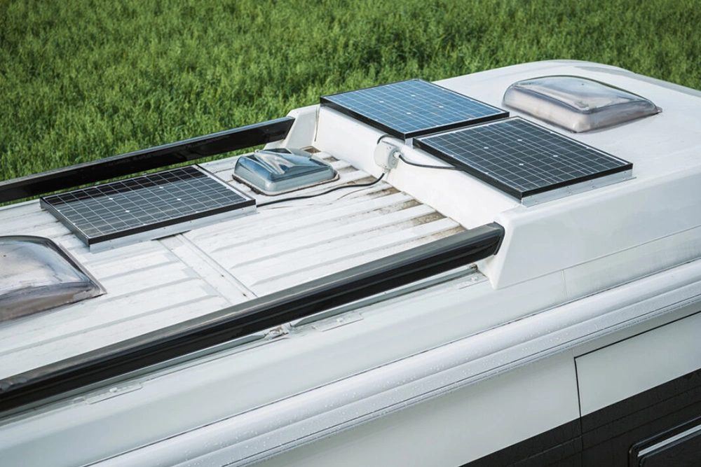 Twee zonnepanelen plat gemonteerd op het dak van een camper, met kabeldoorvoer op de voorgrond.
