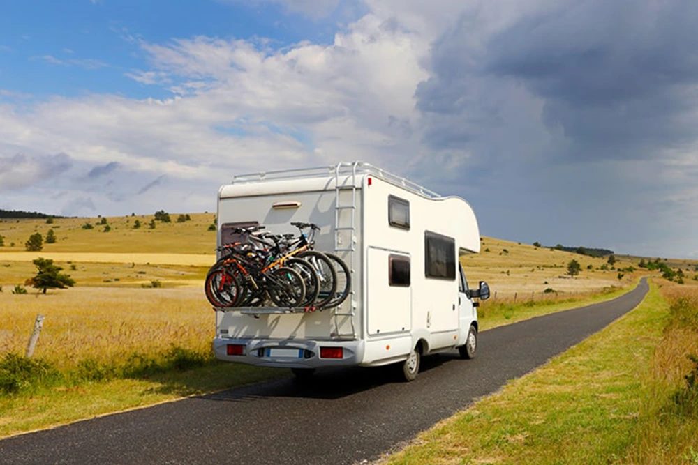 Handen bij een betaalautomaat op een camperplaats met een camper op de achtergrond.